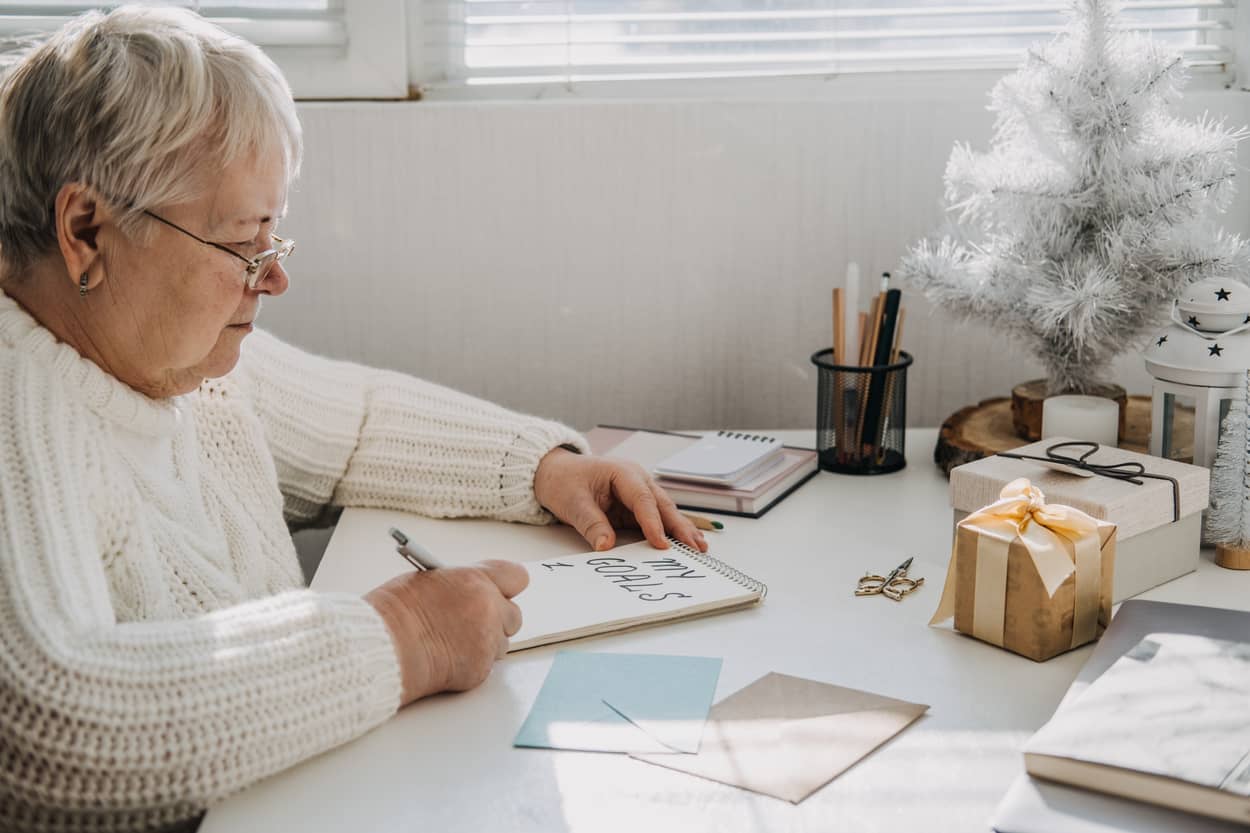 An senior woman writing Goals on a paper.
